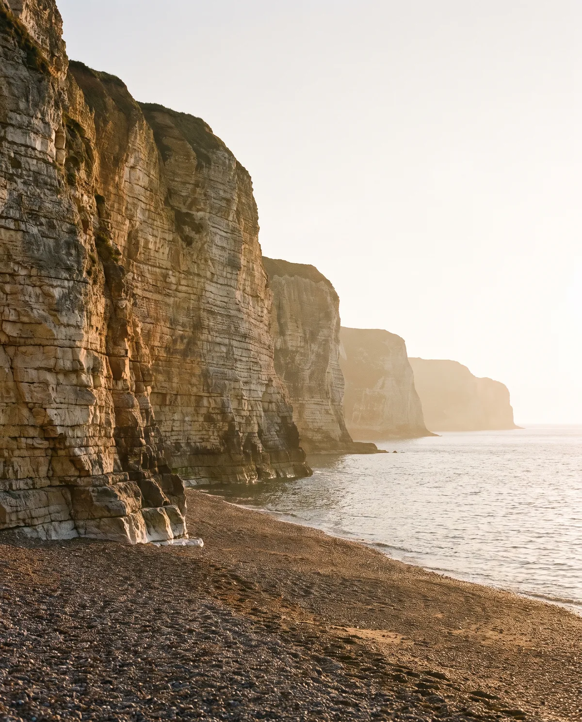 Layered sedimentary sea cliffs above a shingle beach at golden hour